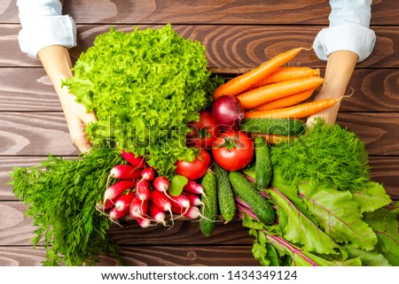 Overhead shot of woman’s hands holding wooden box with vegetables