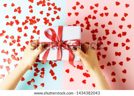 Female hands holding gift box with ribbon on blue and pink background, top view