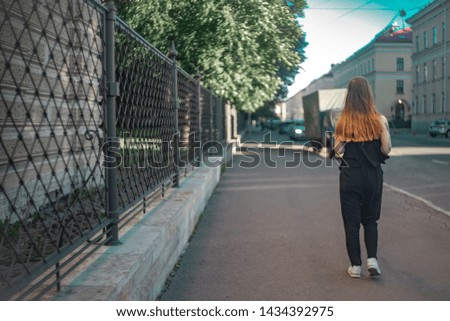red-haired girl walks along the alley along the iron mesh fence