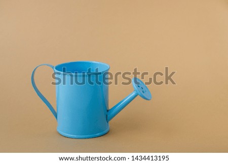 Toy iron blue watering can against a light brown background. Place for text. Agriculture concept.