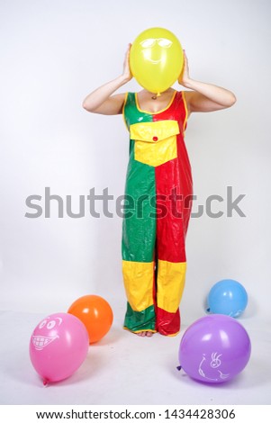 cute chubby girl with short blonde hair and plus size figure in bright colored PVC jumpsuit posing with air balloons on white background alone. playful young woman in halloween good clown costume.