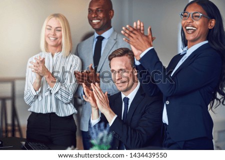 Smiling group of diverse businessmen and businesswomen clapping together while watching a presentation in an office