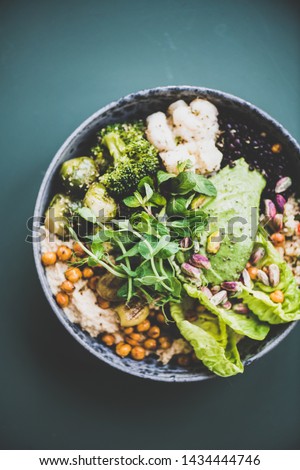 Healthy dinner or lunch at home. Vegan superbowl or Buddha bowl with hummus, vegetable, fresh salad, beans, couscous and avocado on dark background, top view