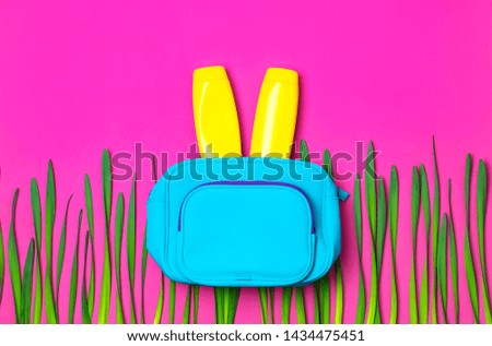 Female cosmetics bag, cosmetic products, sunscreen cream, green leaves on bright pink fuchsia background top view flat lay. Minimalism cosmetics style. Creative concept of hare or rabbit