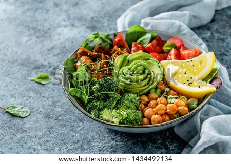 Buddha bowl salad with baked sweet potatoes, chickpeas, broccoli, tomatoes, greens, avocado, pea sprouts on light blue background with napkin. Healthy vegan food, clean eating, dieting, closeup Royalty-Free Stock Photo #1434492134