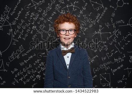 Happy smart kid in blue school suit on blackboard background with science formulas