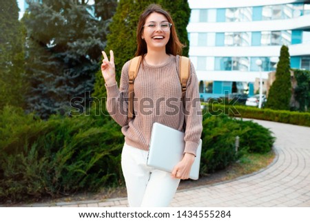 Image of funny attractive girl pouting and showing v-sign.Happy student girl walks down the street in spring around the city
