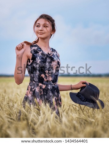 Cute attractive young girl with black hat on wheat field during sunset. Pensive look. Romantic atmosphere.