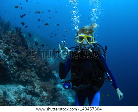 Underwater shoot of a woman diving with scuba by coral reef and showing ok signal