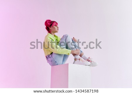 woman with pink hair in sneakers sits on a neon studio cube