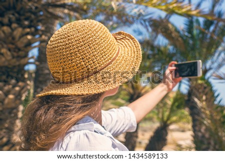 Woman in the straw hat taking selfie picture or video using smartphone in the palm forest. Seychelles islands