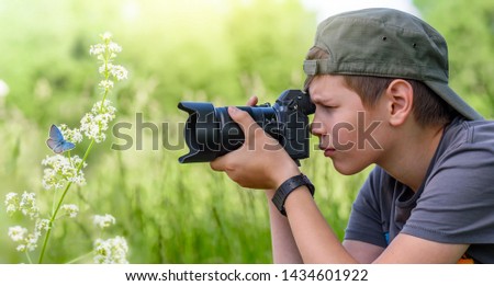 Boy, twelve years old, shooting blue butterfly on the wild flower on nature in summer day