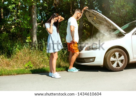 The young couple broke down the car while traveling on the way to rest. They are trying to fix the broken by their own or should hitchhike, getting nervous. Relationship, troubles on the road