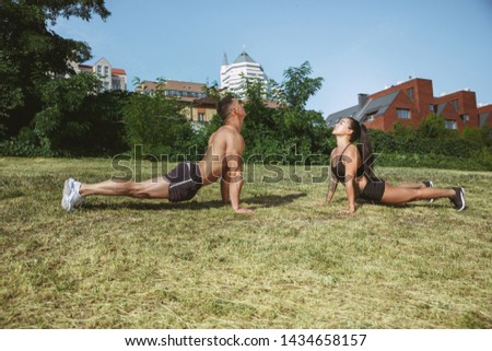 A muscular athletes doing workout at the park. Gymnastics, training, fitness workout flexibility. Summer city in sunny day on background field. Active and healthy lifestyle, youth, bodybuilding.