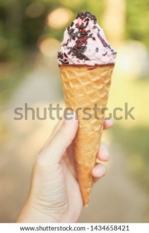 Pink chocolate ice cream in waffle horn in female hand on hot sunny summer day.