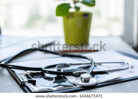 Doctor’s office desk close up with stethoscope, patient’s card, laptop and plant in a pot. Medicine and health concept.
