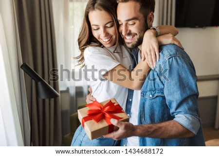Beautiful young couple in love at home, celebrating with a gift box exchange, hugging