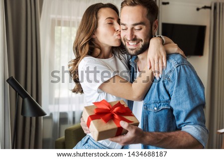 Beautiful young couple in love at home, celebrating with a gift box exchange, kissing