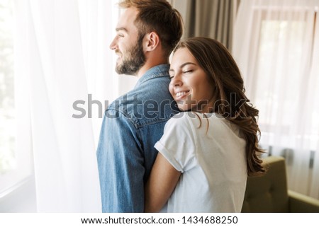 Beautiful young couple in love at home, standing at the window, embracing Royalty-Free Stock Photo #1434688250