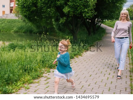 Mother and little daughter walking in city park.