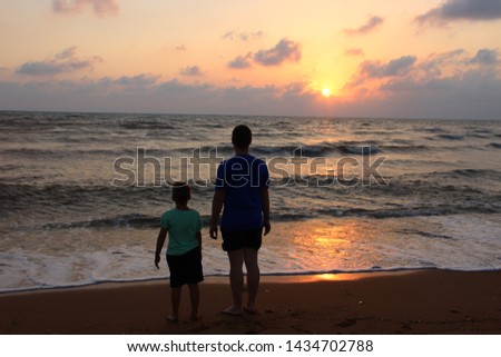 Dad and son are standing on the beach at sunset. against the backdrop of waves and a pink sunset. holding hand happy family and summer vacation Royalty-Free Stock Photo #1434702788
