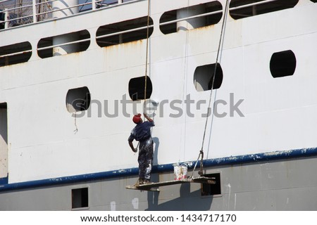 
a man in work clothes is painting a ship. ship repair in the open sea Royalty-Free Stock Photo #1434717170