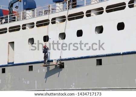 
a man in work clothes is painting a ship. ship repair in the open sea Royalty-Free Stock Photo #1434717173