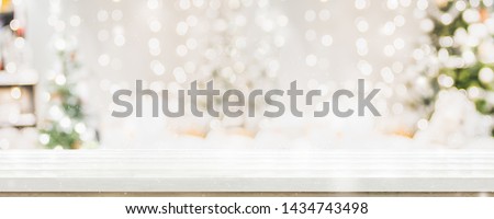 Empty white wold table top with abstract warm living room decor with christmas tree string light blur background with snow,Holiday backdrop,Mock up banner for display of advertise product