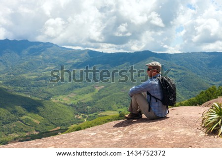 Tourist man sits on a cliff edge on the top of mountain with gorgeous view at stunning valley in the subtropical part of Bolivia. Samaipata. Stock photo