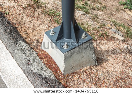 Big steel pole base locked with big bold nut on concrete foundation near the road