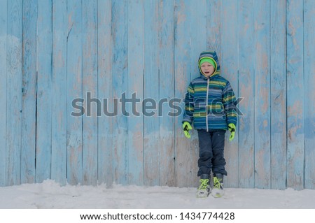 Happy children in winter warm clothes run through snow on eve in village yard. Fence with peeling paint, rustic fun, the joy of  brothers. Children are happy on vacation in the country