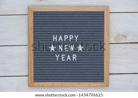English text happy new year and two stars on a felt Board in a wooden frame. white letters on a gray background. letterboard on white wooden background