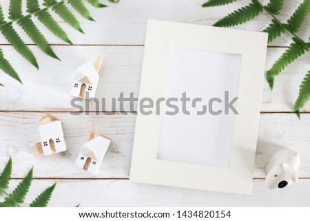 Mock up, Blank White Picture frame with Fern leaf and Miniature white house model on white wooden plank background, minimalist