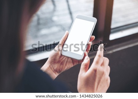 Mockup image of a woman holding white mobile phone with blank desktop screen in cafe