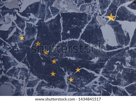 The national flag of the US state Alaska in against a gray wall with cracks and faults on the day of independence in colors of blue ground and yellow stars. Political and dispute, customs and delivery