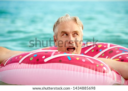 Gray-haired funny man swims on an inflatable circle in the sea