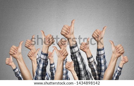 Row of man hands showing thumb up gesture. Agreement and approval group of signs. Human hands gesturing on background of grey wall. Many arms raised together and present popular gesture.