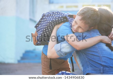 Back to school. Happy mother and son embrace in front of the elementary school. The parent takes the child to primary school. The student goes to study with a backpack. The first day of autumn.