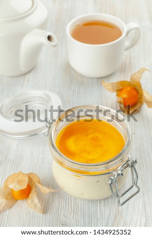 Dessert in a jar with a cup of black tea, served on a total-white background: creamy tiramisu iwth whipped mascarpone, savoyardi and mango sauce