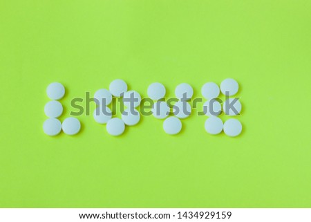 White pills in a shape of a word Love on a yellow background. Flat lay, top view, minimalistic style. Vitamins, drugs, dietary supplements.
