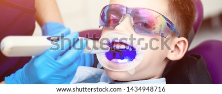 The boy with goggles in the dental chair. Mouth directed lightpolymerization lamp with blue light for sustainable fillings.