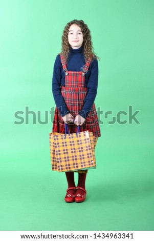 Child with a yellow packaging checkered texture  isolated on green background. Holiday present, shopping.  Happy girl with long curly hair. High resolution photo. Full depth of field.