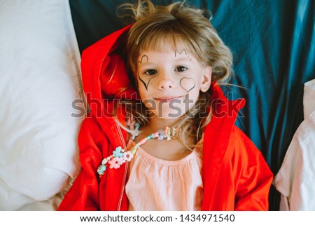 Portrait of a little girl lying on the bed  with painted hearts on her face