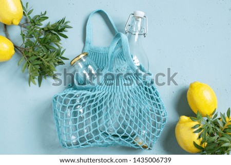 Blue background with mesh bag, glass bottle and jars decorated with fresh lemons. Zero waste, eco friendly or plastic free lifestyle concept, copy space