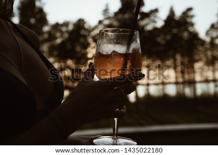 A girl holds a glass with a cocktail. The picture was taken in the spa center by the pool, against the backdrop of the sunset.
