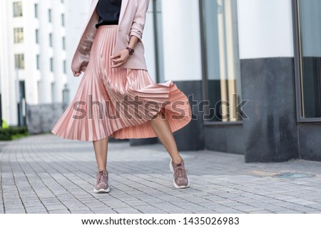 Pleated skirt coral color and sneakers. The girl is very dynamic posing on the street, the skirt is developing. Royalty-Free Stock Photo #1435026983