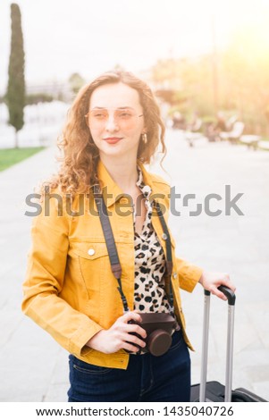 Millennial teen with red hair is traveling the world,she is arrived in a new city, and look for accommodation with her camera around the neck, travel instagram blogger theme.