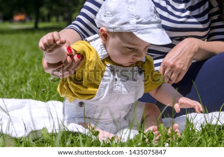 Baby boy touching green grass for the first time.Mother hand helping infant child to sit on the blanket in the park 