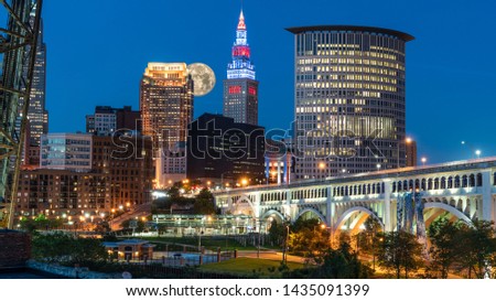 Big Moon Rising Over Cleveland Ohio Along The Cuyahoga River With Bright Lights And Iconic Bridge.