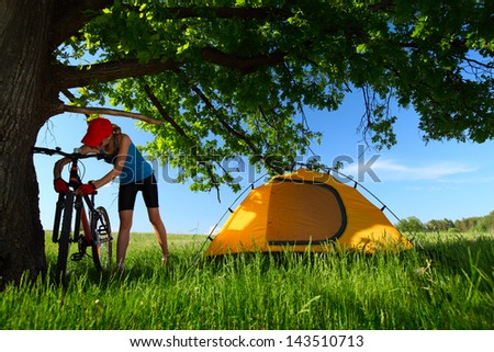 Young lady maintaining bicycle on a meadow with green grass